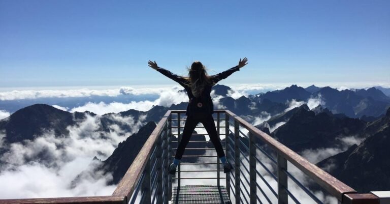 A woman stands on a viewing platform in Vysoké Tatry, Slovakia, surrounded by clouds and mountains, embracing freedom.