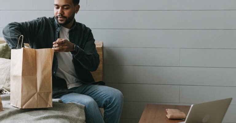 Young man unpacking delivery bag in modern home setting, seated near laptop.