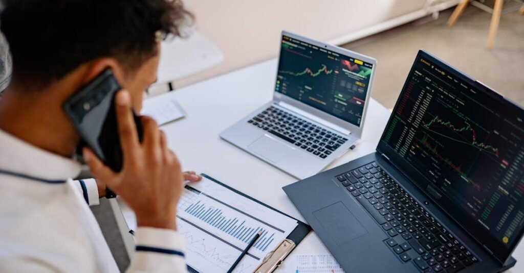 Man analyzing stock market charts on laptops while talking on a cellphone.