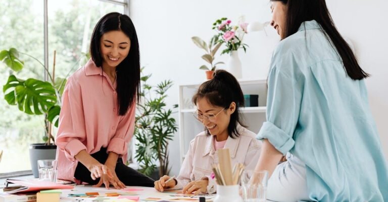 Three women collaborating creatively with colorful materials in a bright office setting.